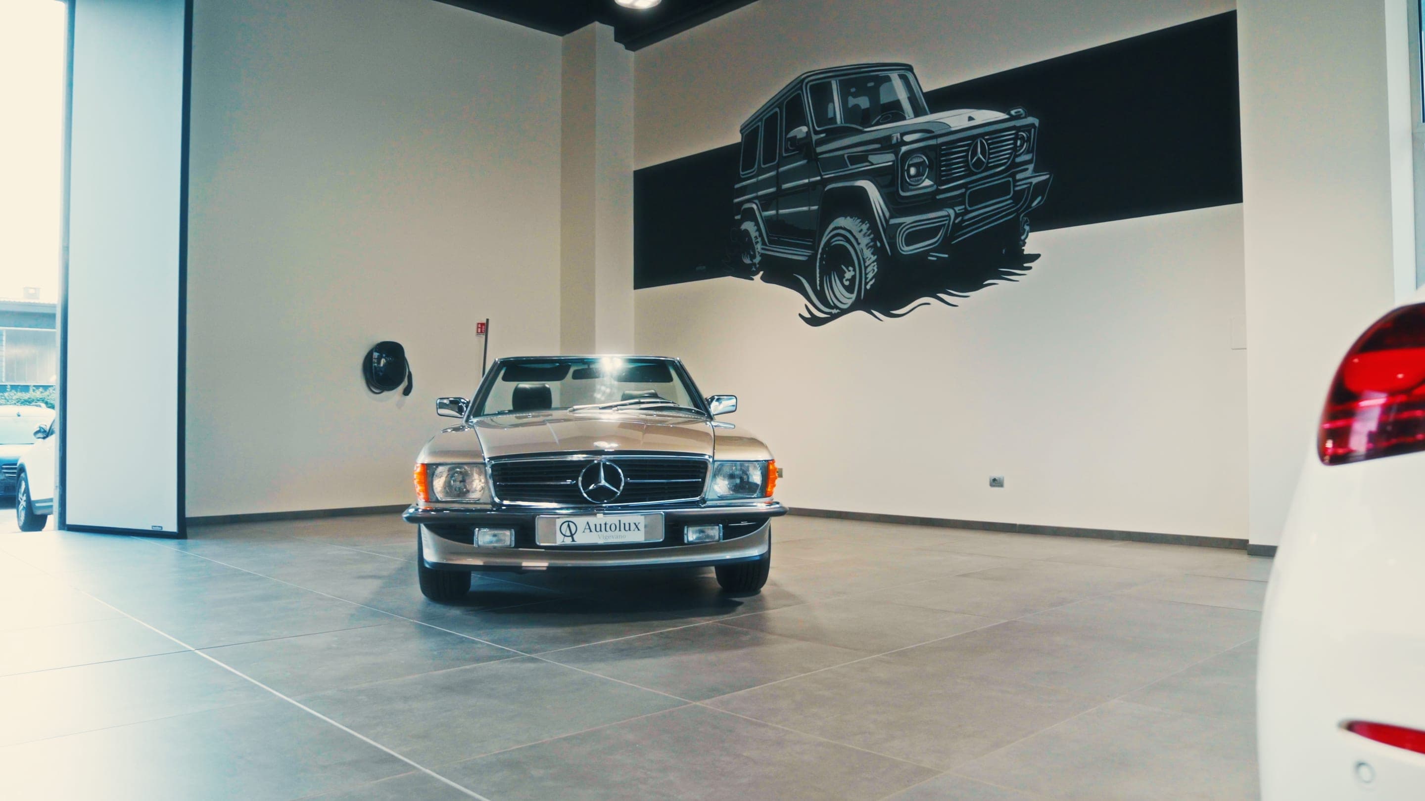 Una Mercedes-Benz SL d’epoca con la targa Autolux nello showroom di Vigevano, sotto il disegno della Classe G